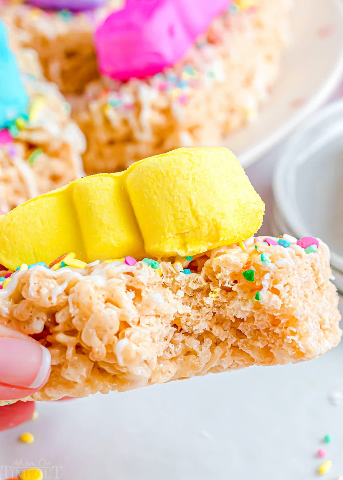 a treat held up with a bite taken out of it. a yellow peep is on top of the rice krispie treat.