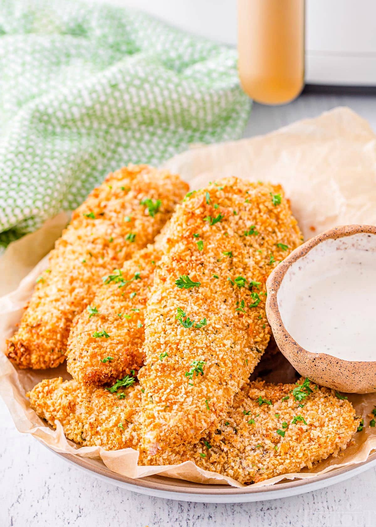 chicken tenders made in the air fryer plated and topped with parsley. air fryer can be seen in the background.