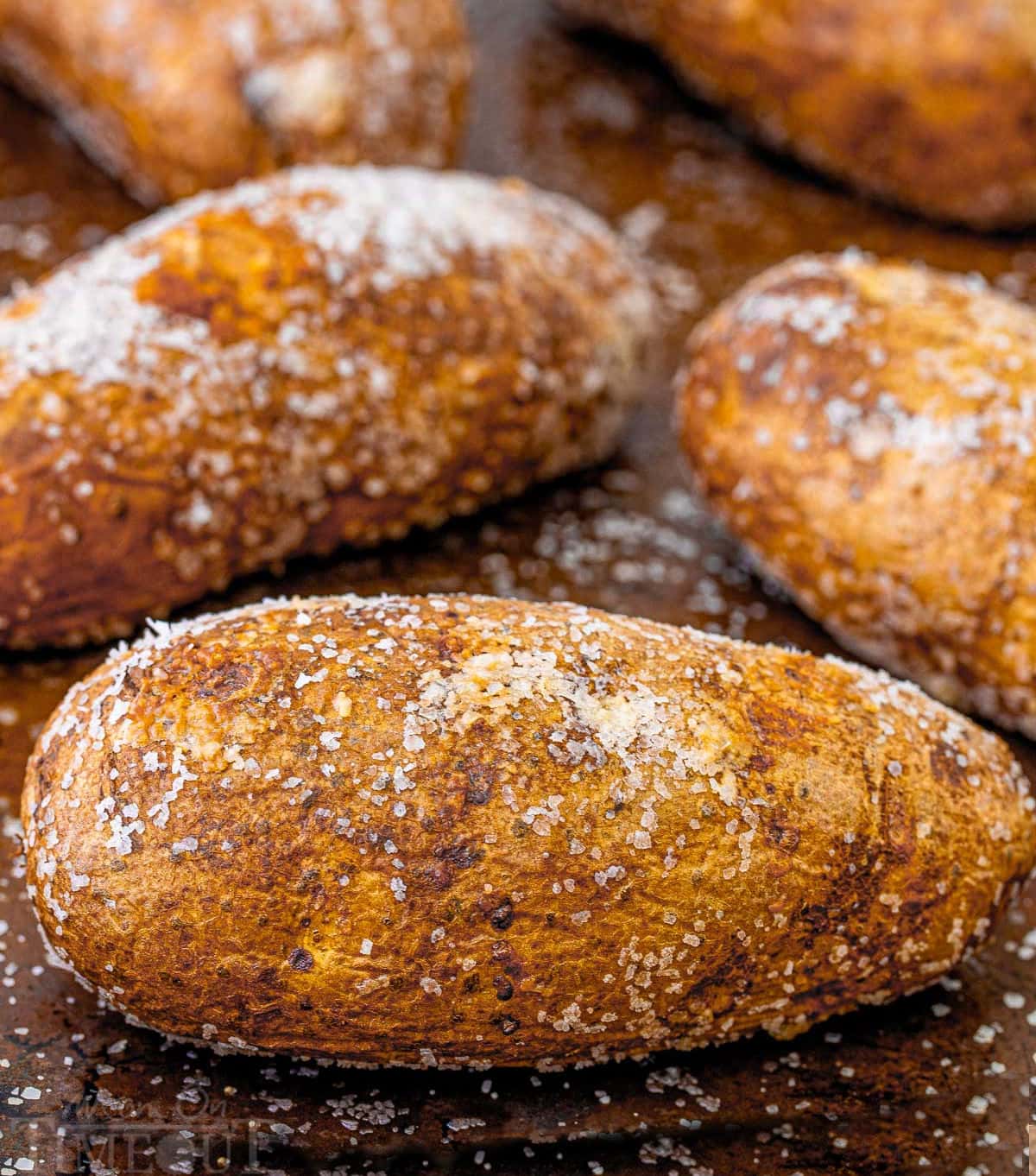 five baked potatoes sitting on a baking sheet liberally salted.