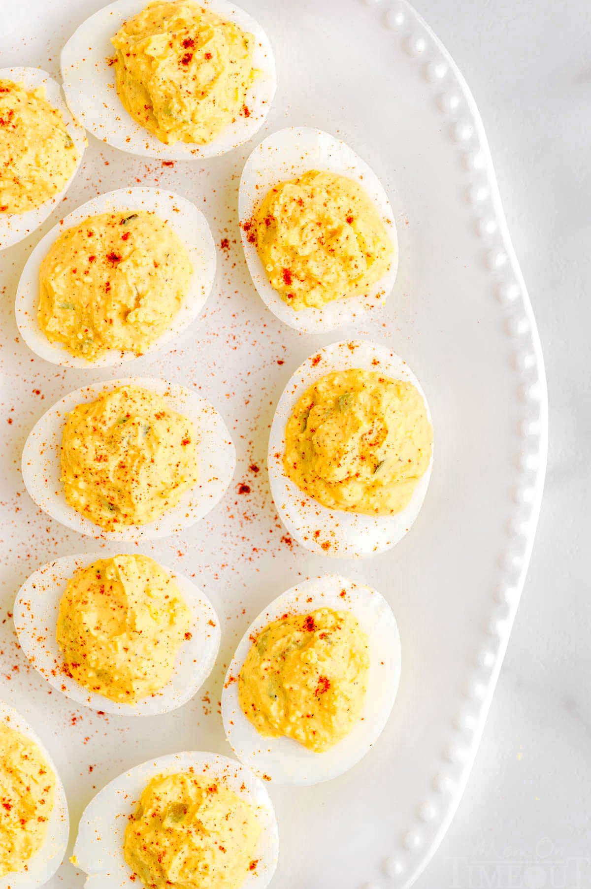 top down look at half of a white platter topped with classic deviled eggs topped with paprika.