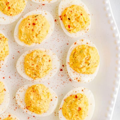 close up of deviled eggs on a white tray with a beaded edge dusted with paprika.