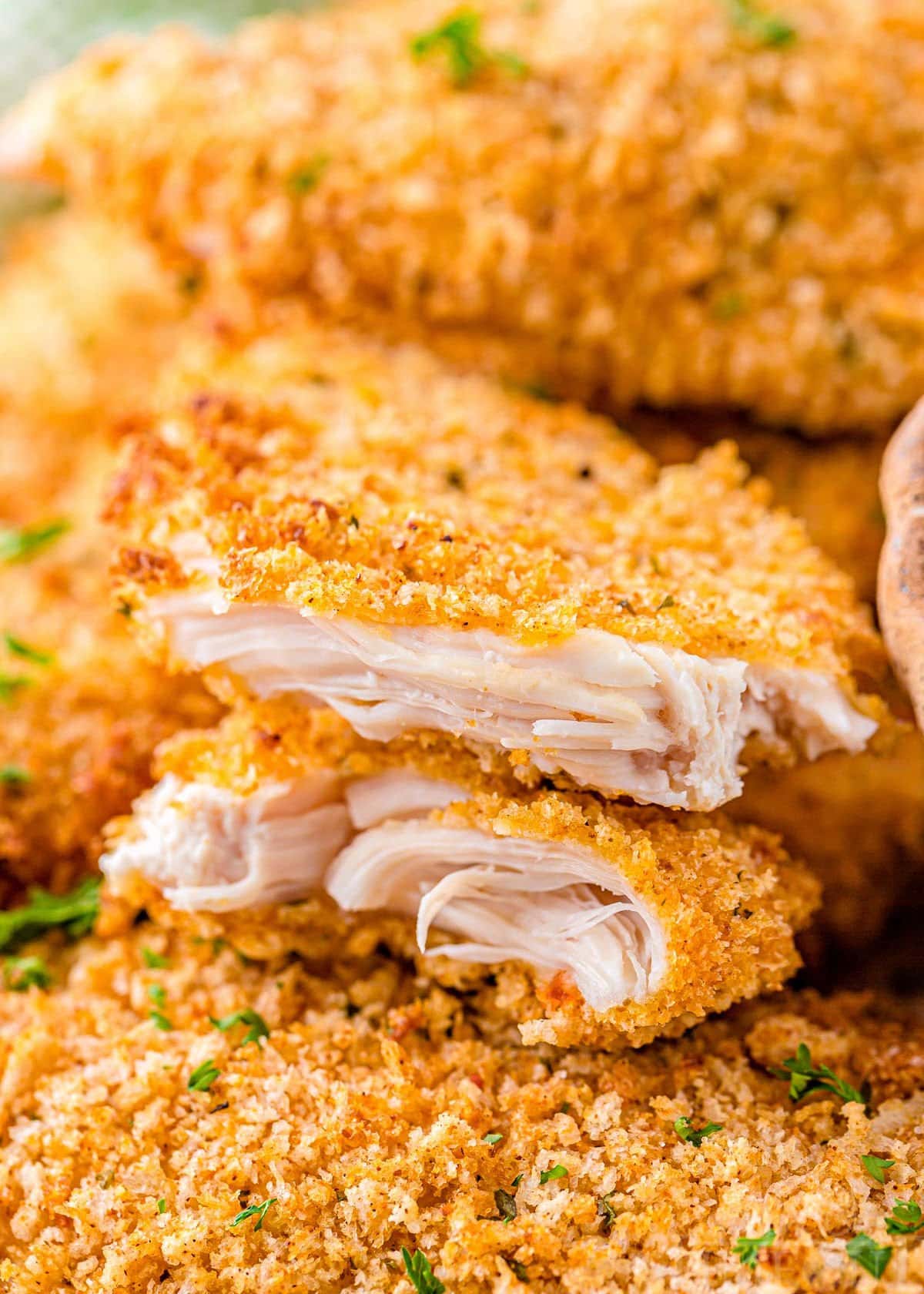 chicken tender torn in half so you can see the cooked chicken and breading. Torn tender is sitting on a pile of more chicken tenders.