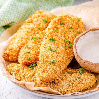 chicken tenders made in the air fryer plated and topped with parsley. air fryer can be seen in the background.