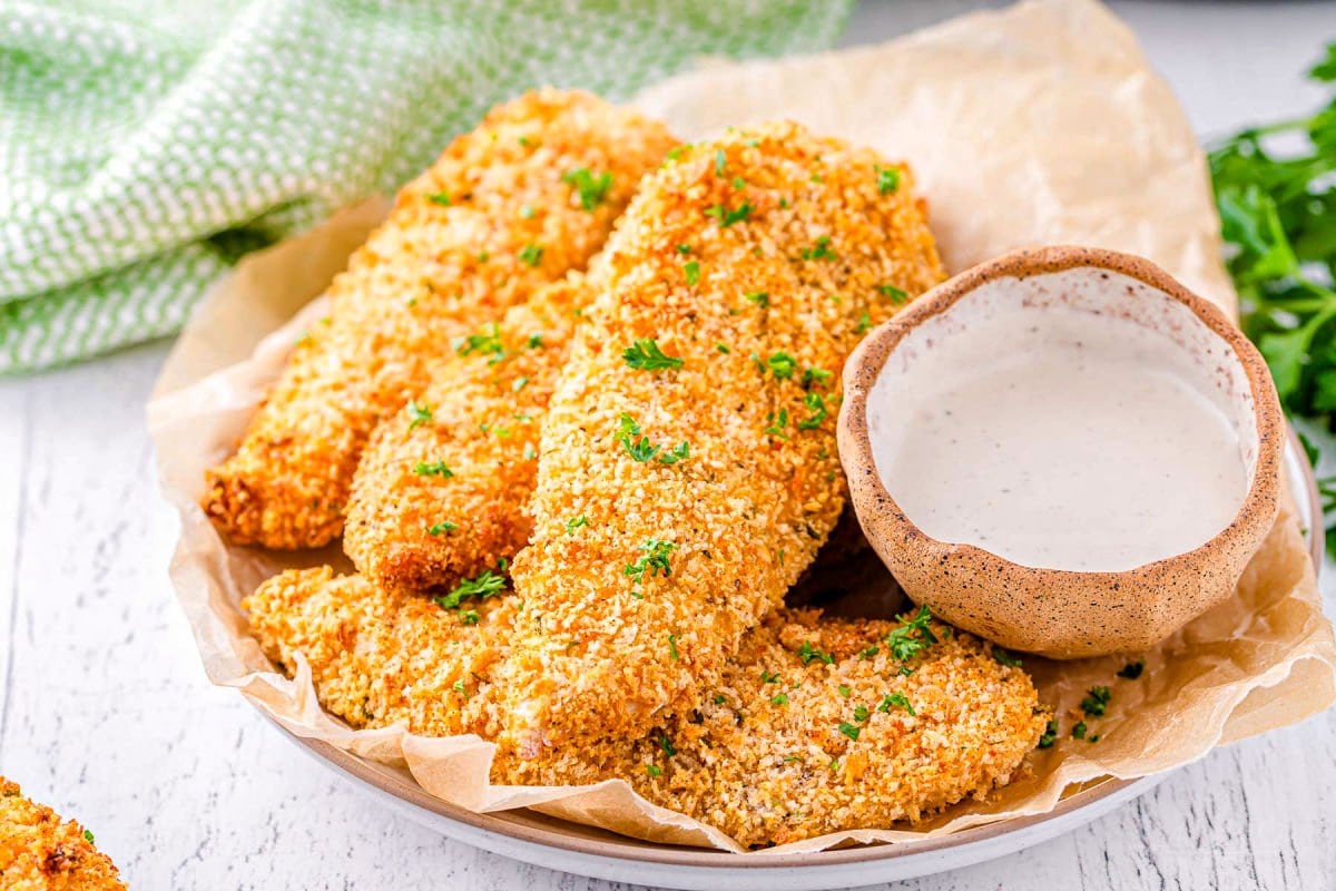 chicken tenders made in the air fryer plated and topped with parsley. air fryer can be seen in the background.