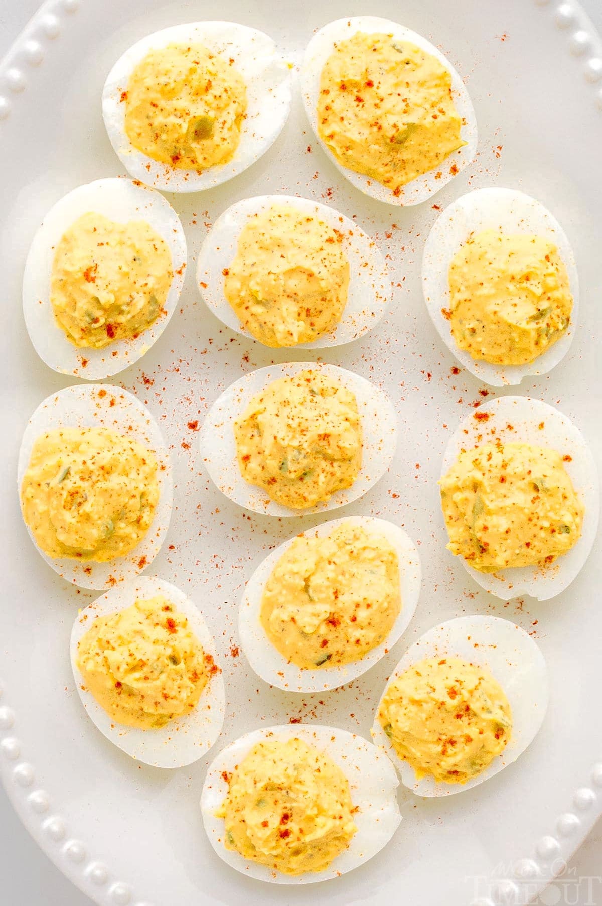 close up of deviled eggs on a white tray with a beaded edge dusted with paprika.