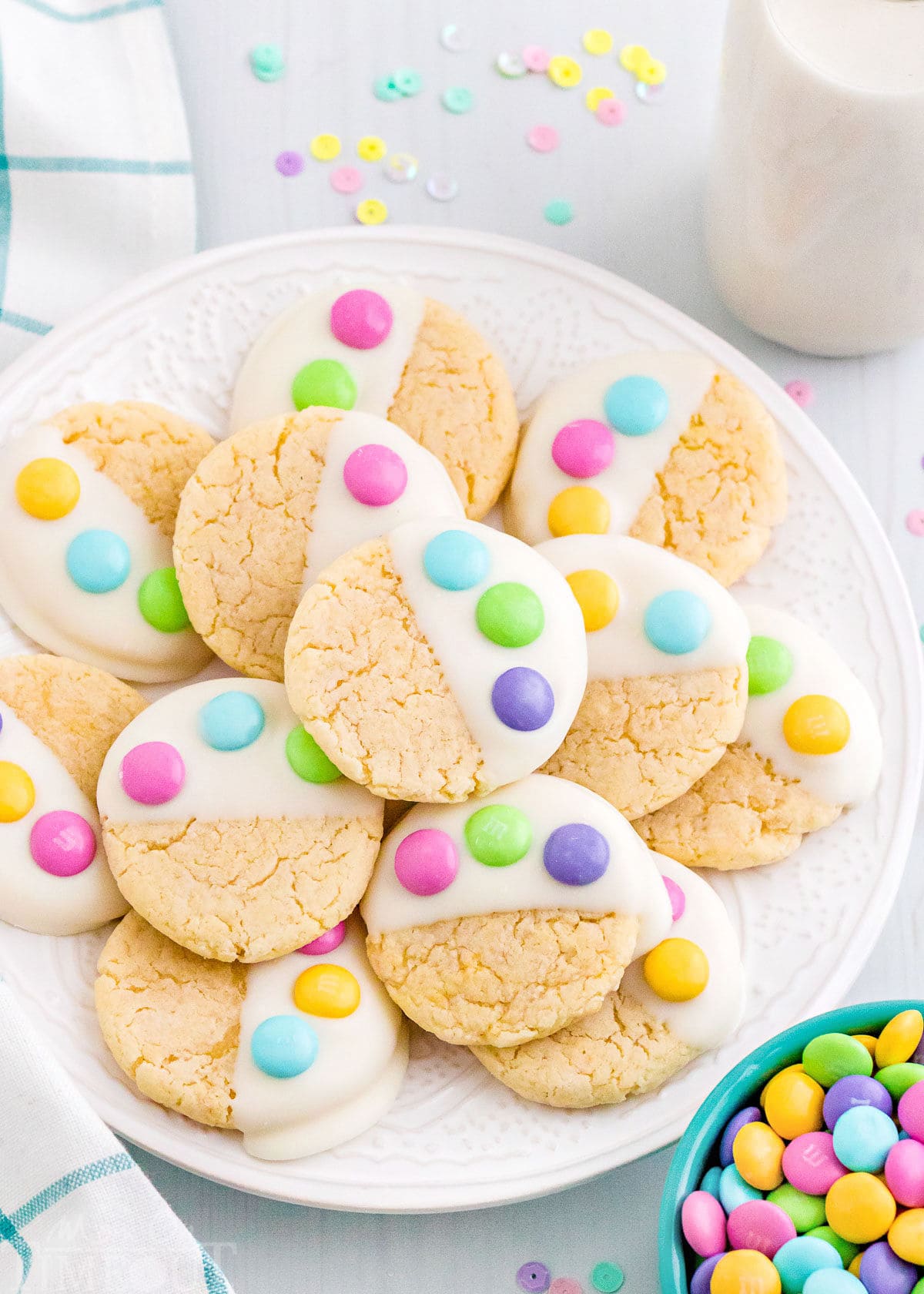 white plate filled with cake mix cookies dipped in candy melts and topped with three m&ms to resemble a bunny paw print. 