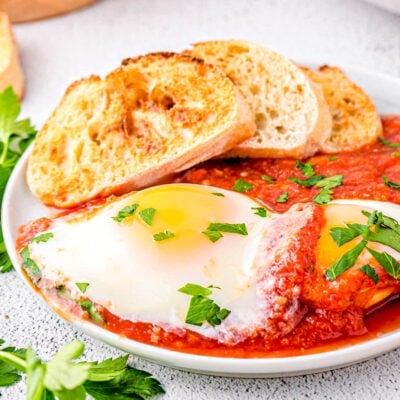 eggs in purgatory plated with extra sauce and nicely toasted crusty bread. The dish is topped with chopped parsley.