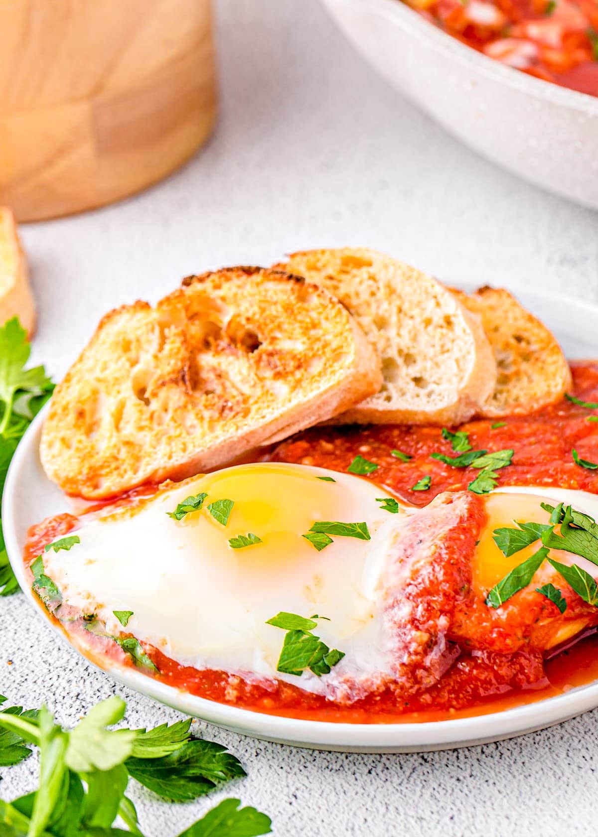 eggs in purgatory plated with extra sauce and nicely toasted crusty bread. The dish is topped with chopped parsley.