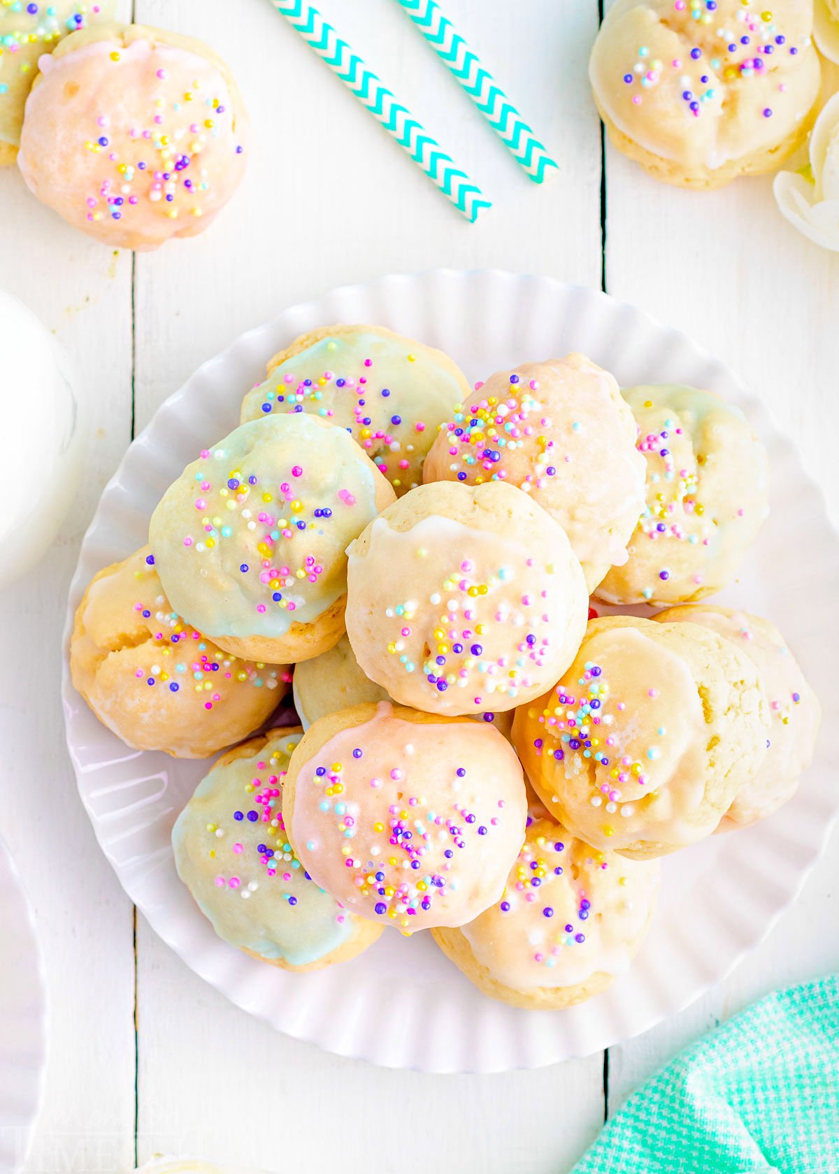 top down view of white plate piled high with cookies topped with pastel glazes and sprinkles. plate is sitting on a white wood backdrop.