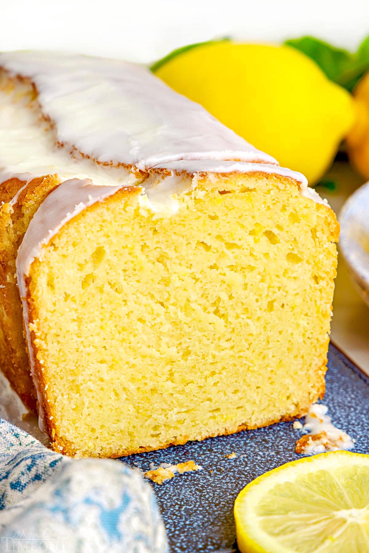 loaf of lemon limoncello cake with limoncello glaze sitting on a blue speckled ceramic board. A few slices have been cut off so you are seeing the crosssection.