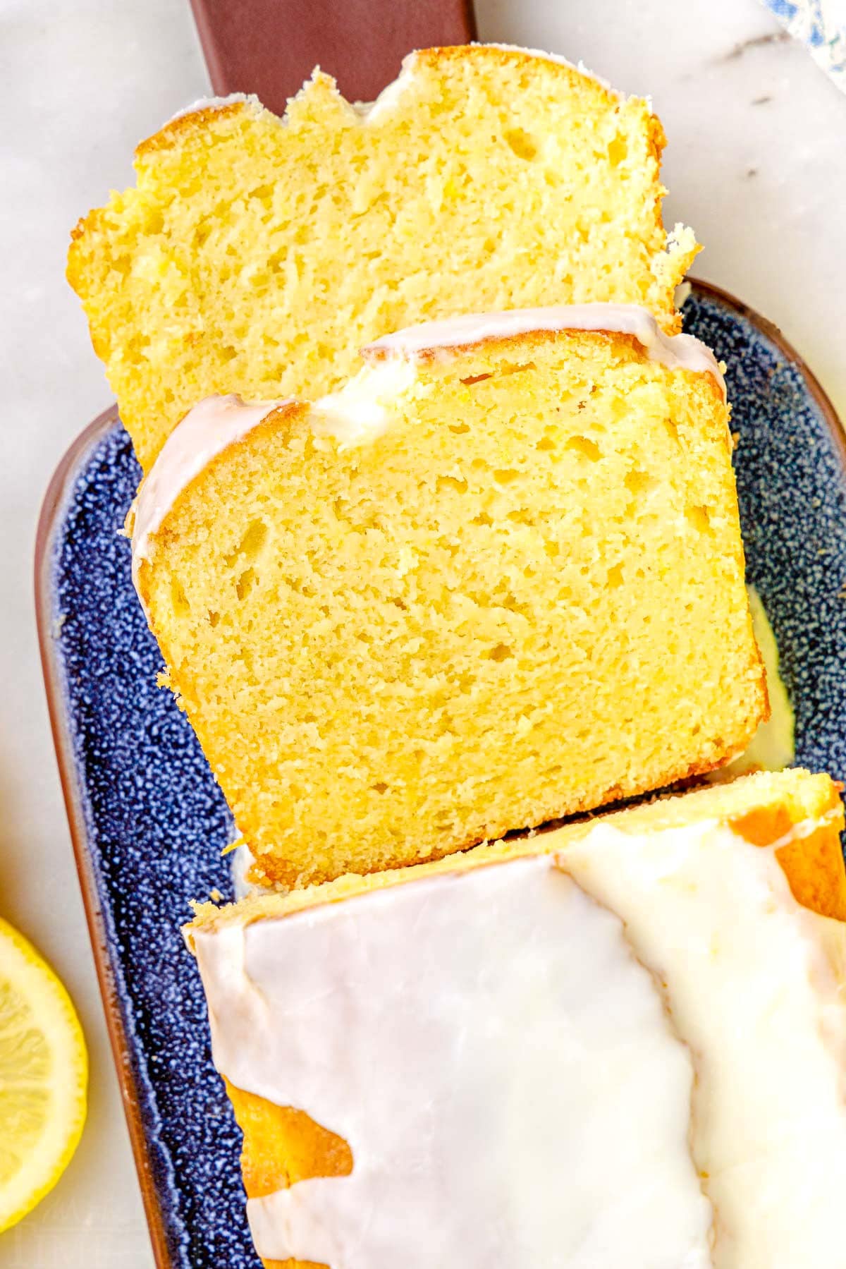 top down look at two slices of limoncello cake and the rest of the loaf cake on a blue glazed clay cutting board.