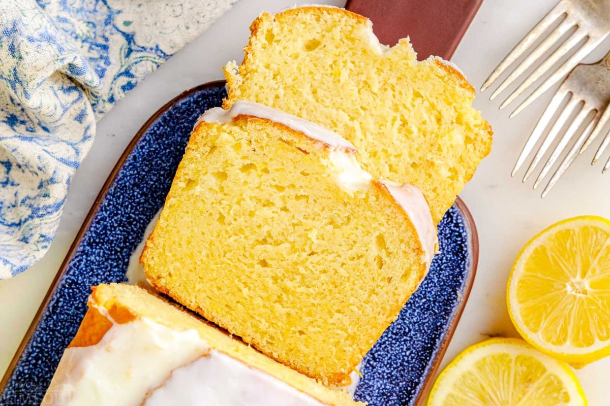 top down look at two slices of limoncello cake on a blue glazed clay cutting board. you can see the rest of the loaf and the glaze on top as well.