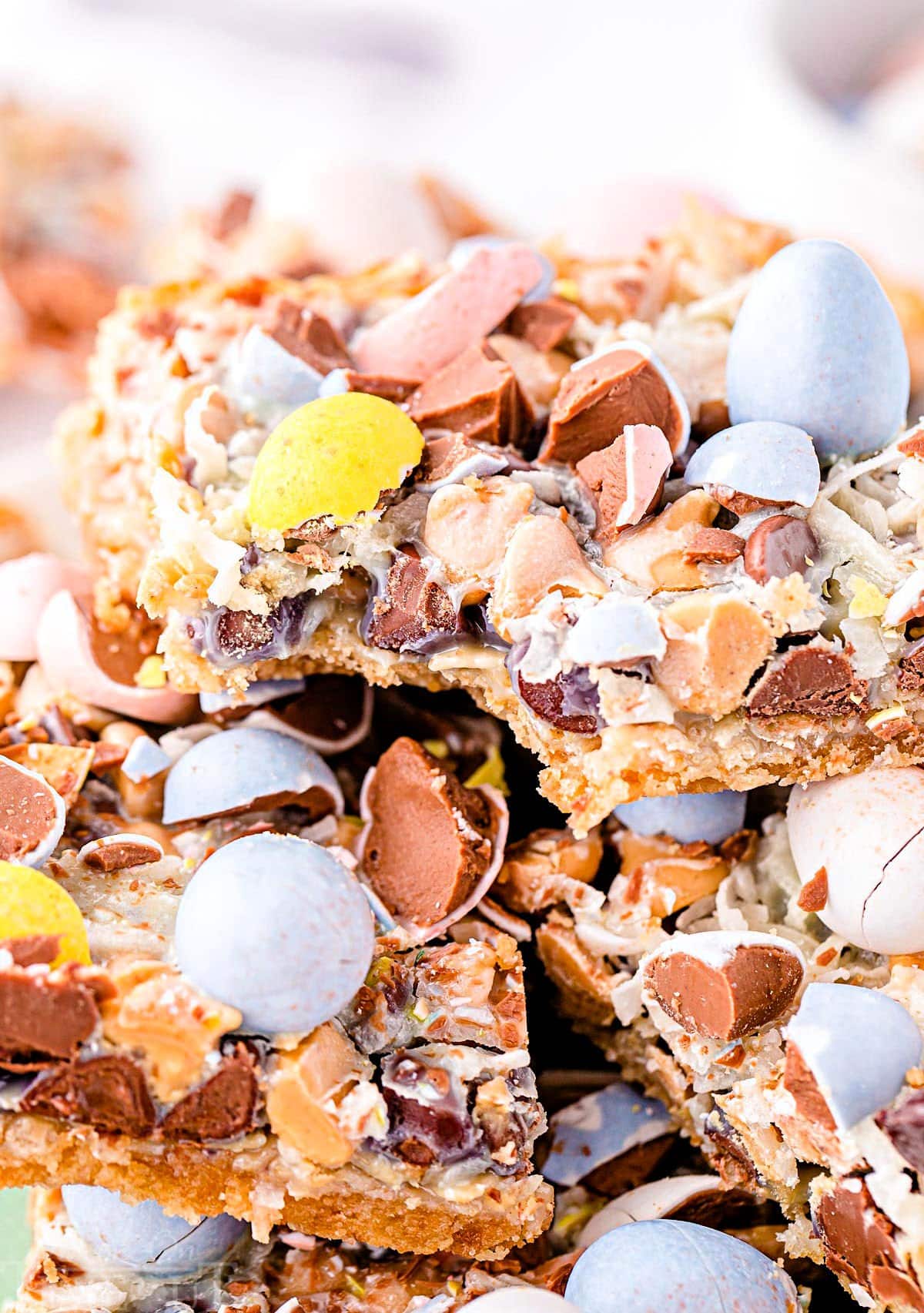 cadbury eggs seven layer bars stacked on a plate with the top bar having a bite taken.