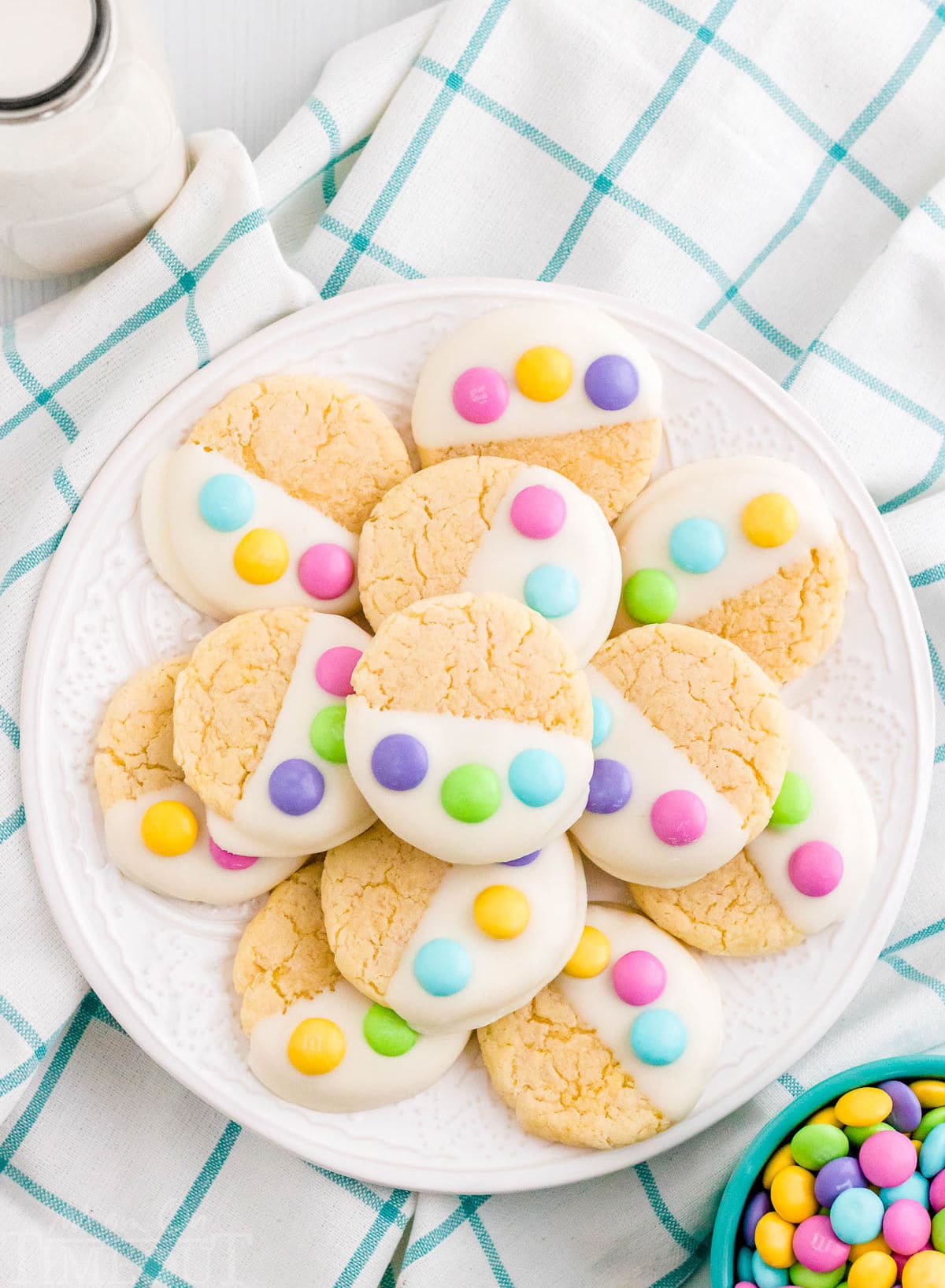 white plate filled with cake mix cookies dipped in candy melts and topped with three m&ms to resemble a bunny paw print.