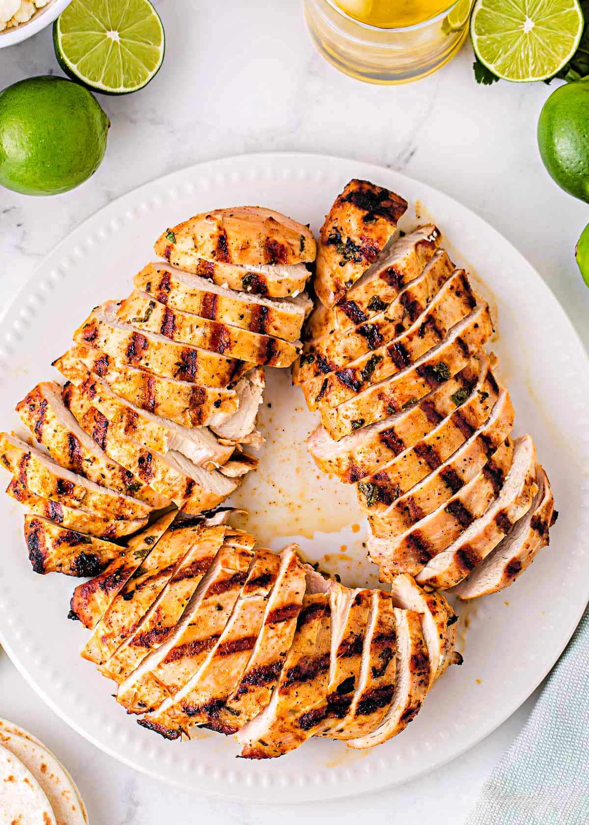 white plate with grilled chicken breasts cut into slices arranged in a circular pattern. Limes can be seen next to the plate.