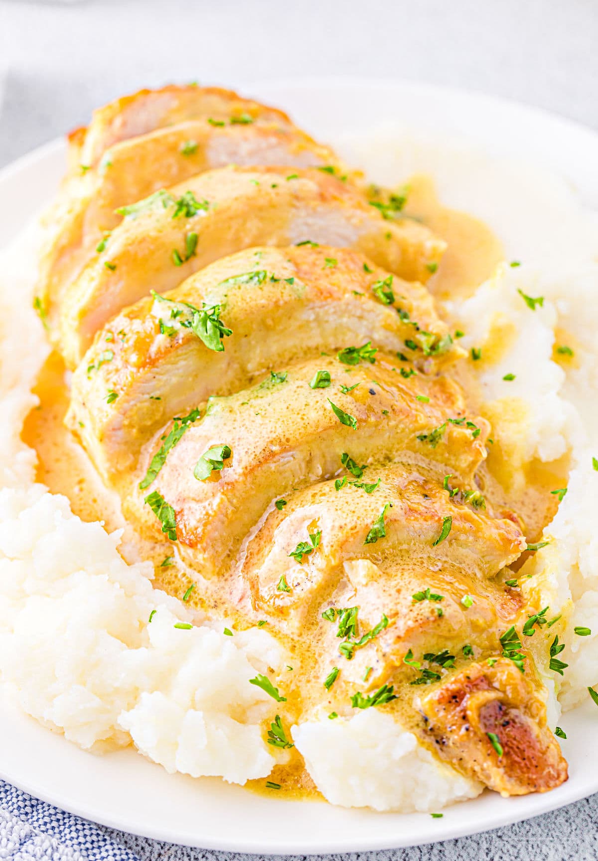 close up look at sliced chicken breast with honey mustard sauce sitting on a bed of mashed potatoes on a white plate.