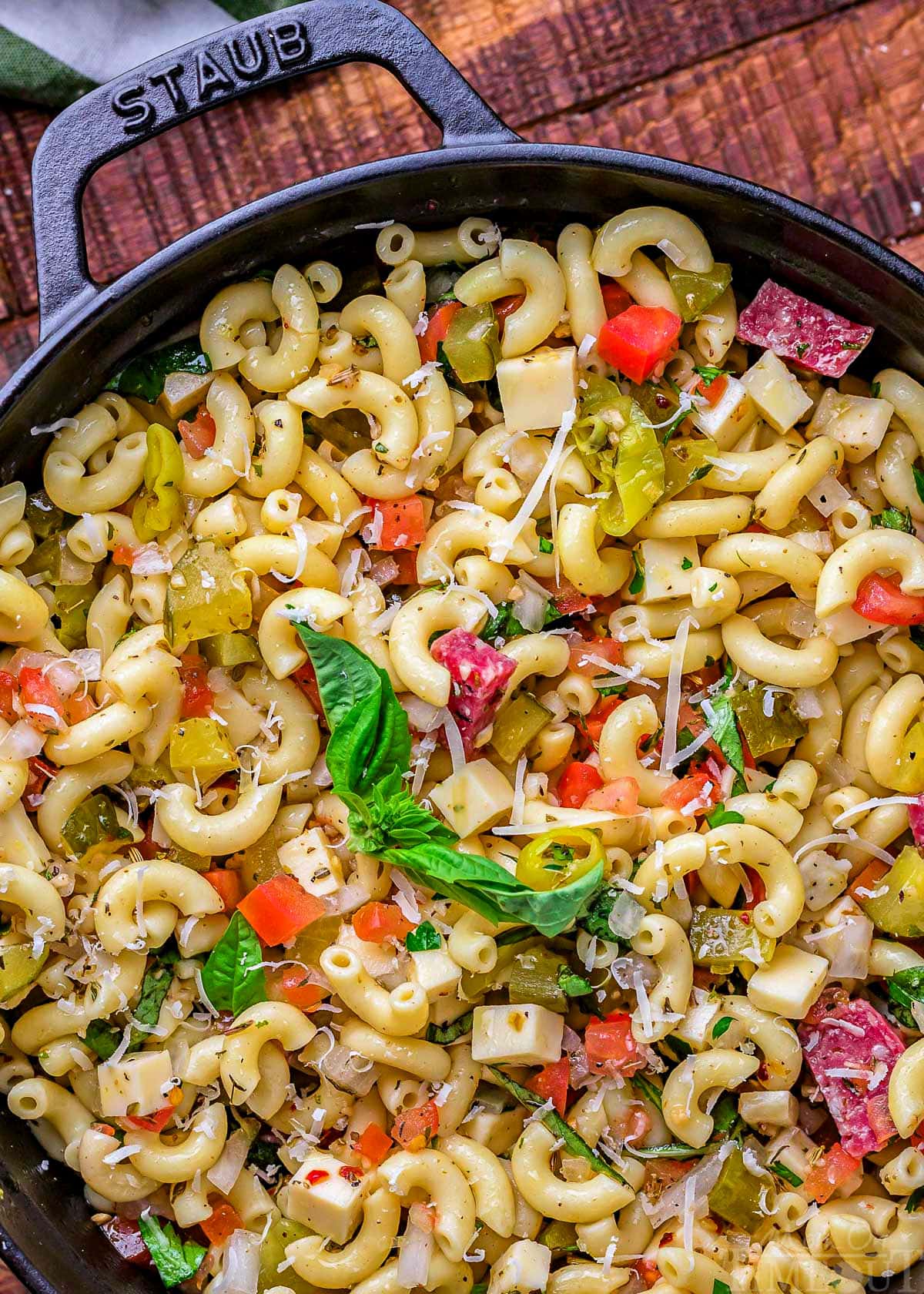 close up of italian pasta salad in a black staub casserole dish ready to be served. garnished with fresh basil.