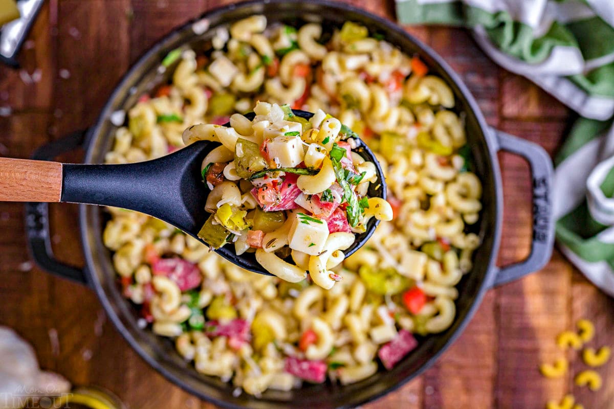spoonful of pasta salad held above the black serving dish .