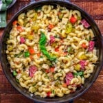 top down look at a large black serving dish with handles filled with pasta salad tossed with Italian dressing. The bowl is on a dark wood surface.