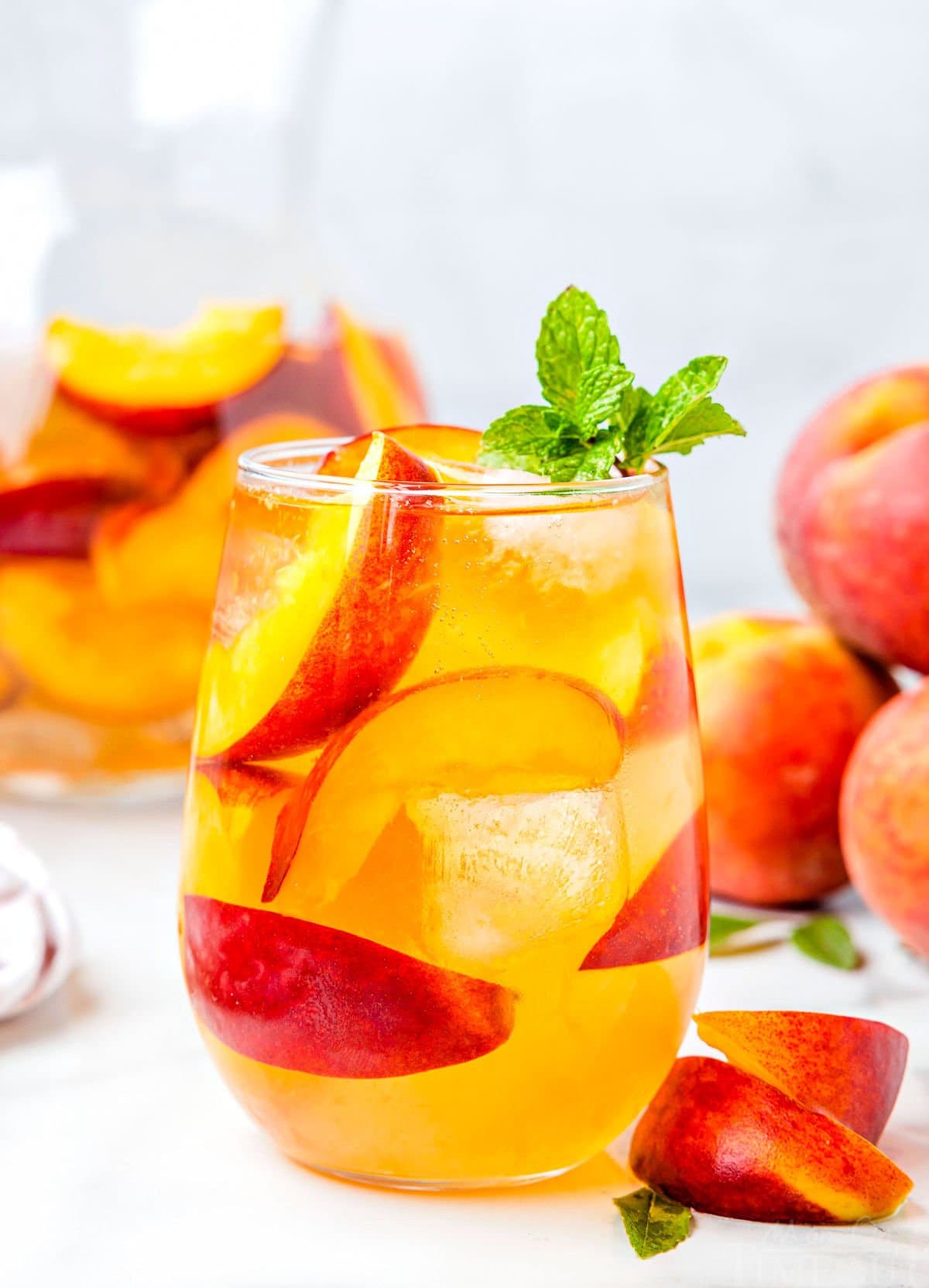 peach sangria recipe made with white wine in stemless wine glass ready to be enjoyed. garnished with mint and fresh peach slices.