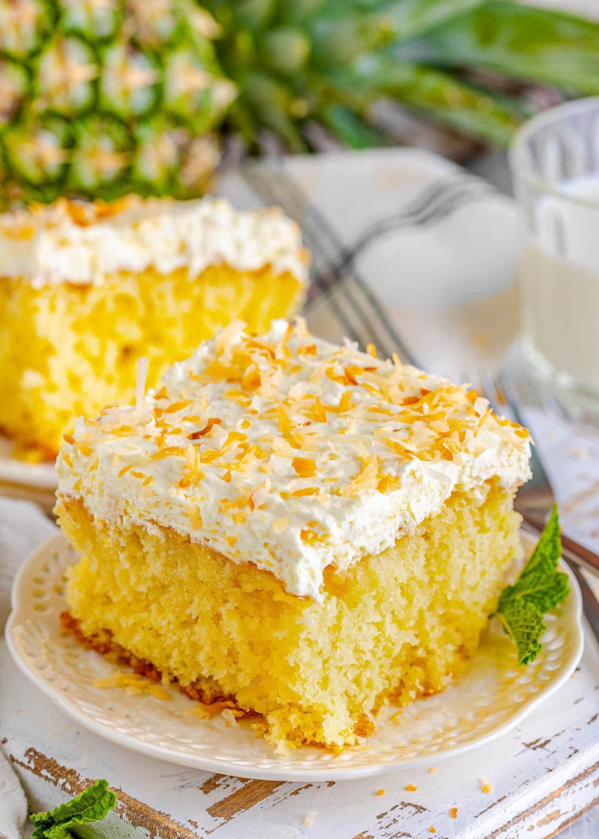 single piece of pina colada poke cake on white plate ready to be enjoyed. topped with a fluffy pineapple coconut frosting and toasted shredded coconut.