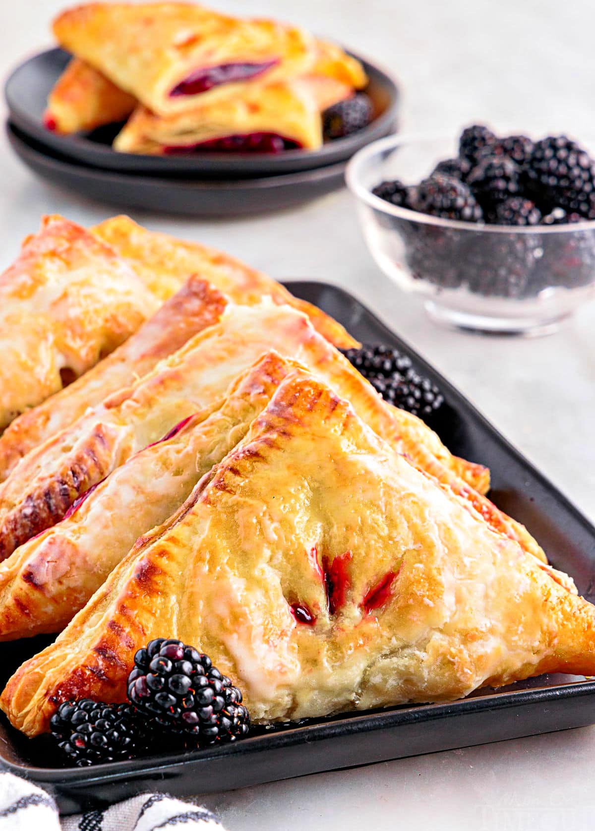 front view of black rectangular plate with turnovers lined up ready to be served. bowl of blackberries is off the the right side.