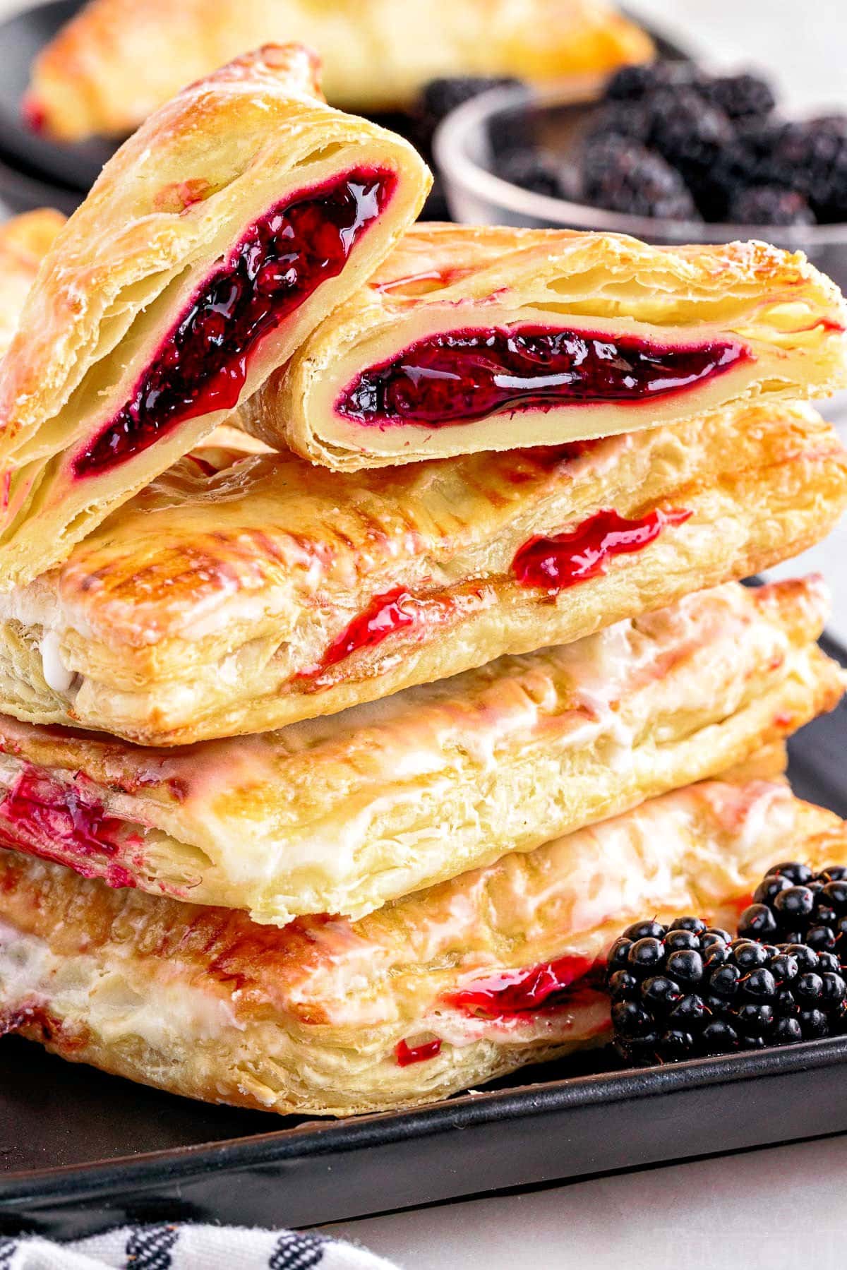 blackberry turnovers stacked on a black plate and top pastry has been cut in half. 