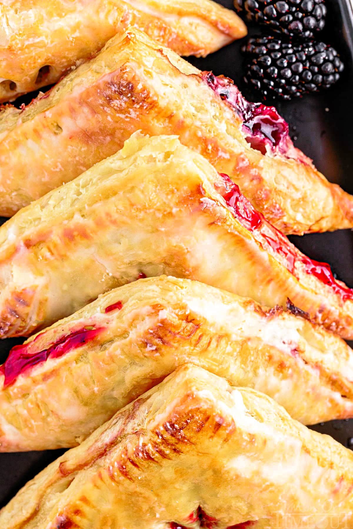 close up look at turnovers with blackberry filling lined up on a black plate.