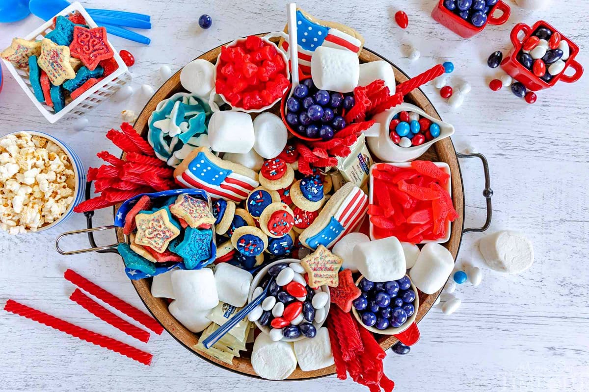 top down look at wood charcuterie board loaded with red white and blue desserts for 4th of july. cookies, candy and all sorts of colorful treats.