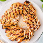 white plate with grilled chicken breasts cut into slices arranged in a circular pattern. Limes can be seen next to the plate.