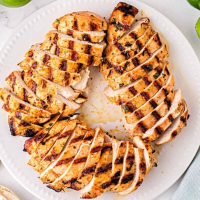 white plate with grilled chicken breasts cut into slices arranged in a circular pattern. Limes can be seen next to the plate.