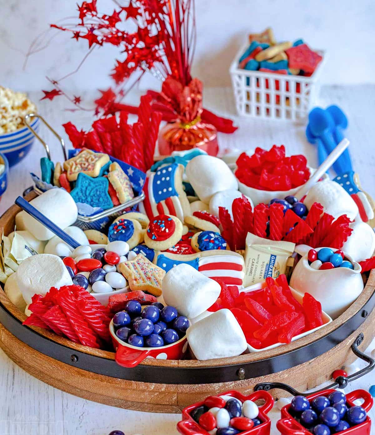 angled front view of round wood board with lots of red, white and blue treats for the holiday. marshmallows, cookies, and candies on the board.
