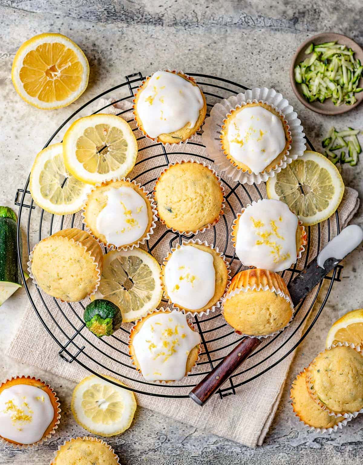 dall'alto in basso guarda i muffin di zucchine glassati fatti con il limone su una griglia di raffreddamento di filo nero con fette di limone sparse.