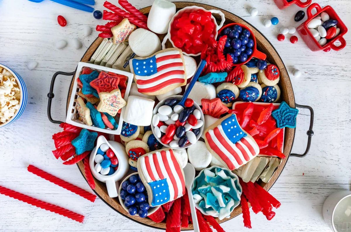 top down look at wood charcuterie board loaded with red white and blue desserts for 4th of july. cookies, candy and all sorts of colorful treats.