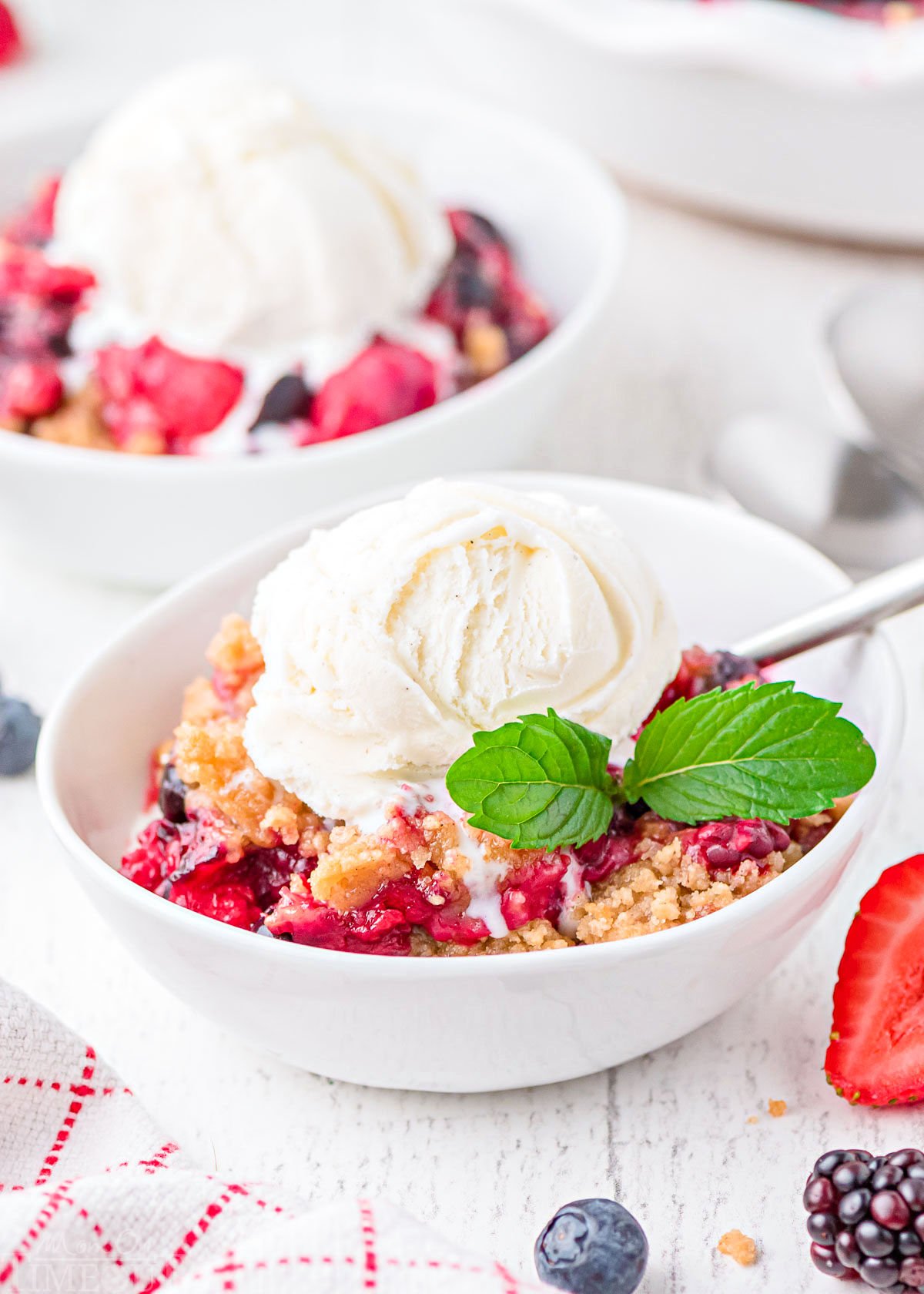 two bowls of berry crumble topped with a scoop of vanilla ice cream in white bowls.