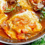 close up look at french onion pork chops in a stainless steel skillet topped with melted and browned cheese. fresh rosemary sprigs are scattered about.