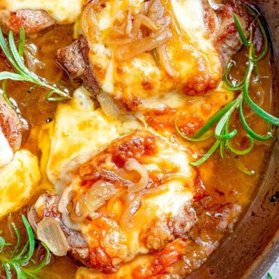 top down look at pork chops in skillet made with French Onion soup flavors. Melted cheese is browned on top.