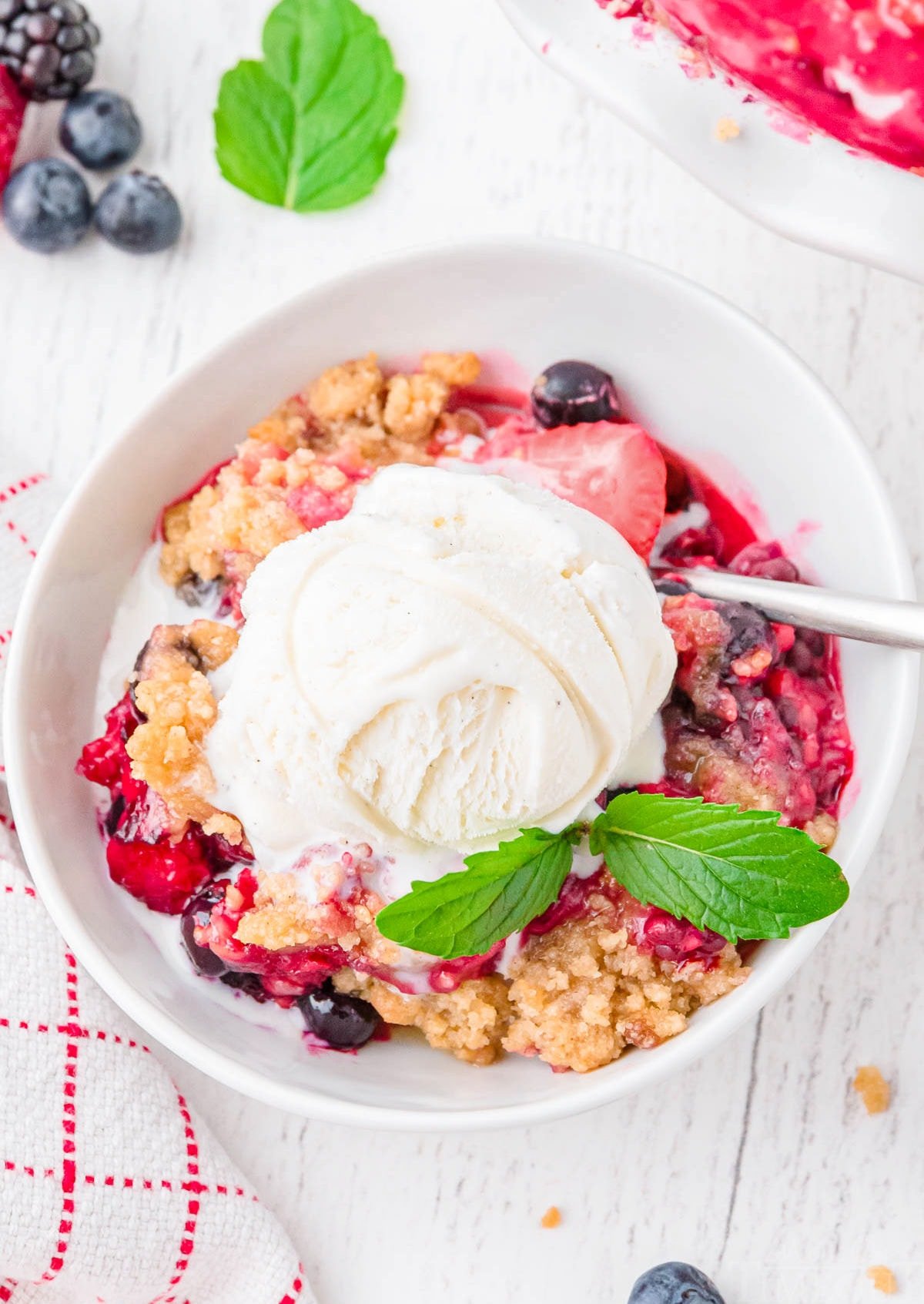 top down view of white bowl filled with berry crisp and topped with vanilla ice cream.