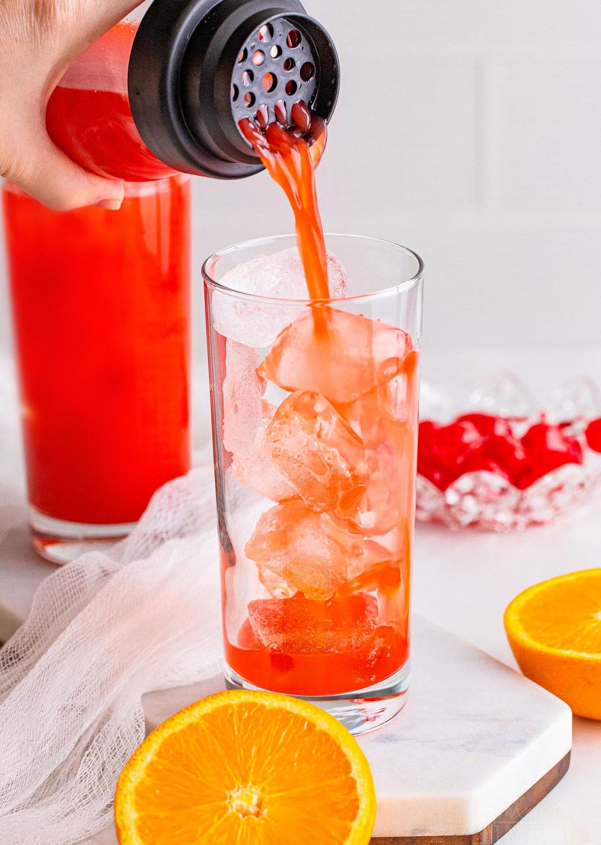 alabama slammer cocktail being poured into a tall ball glass with ice in it. one drink has already being poured and can be seen in the background.