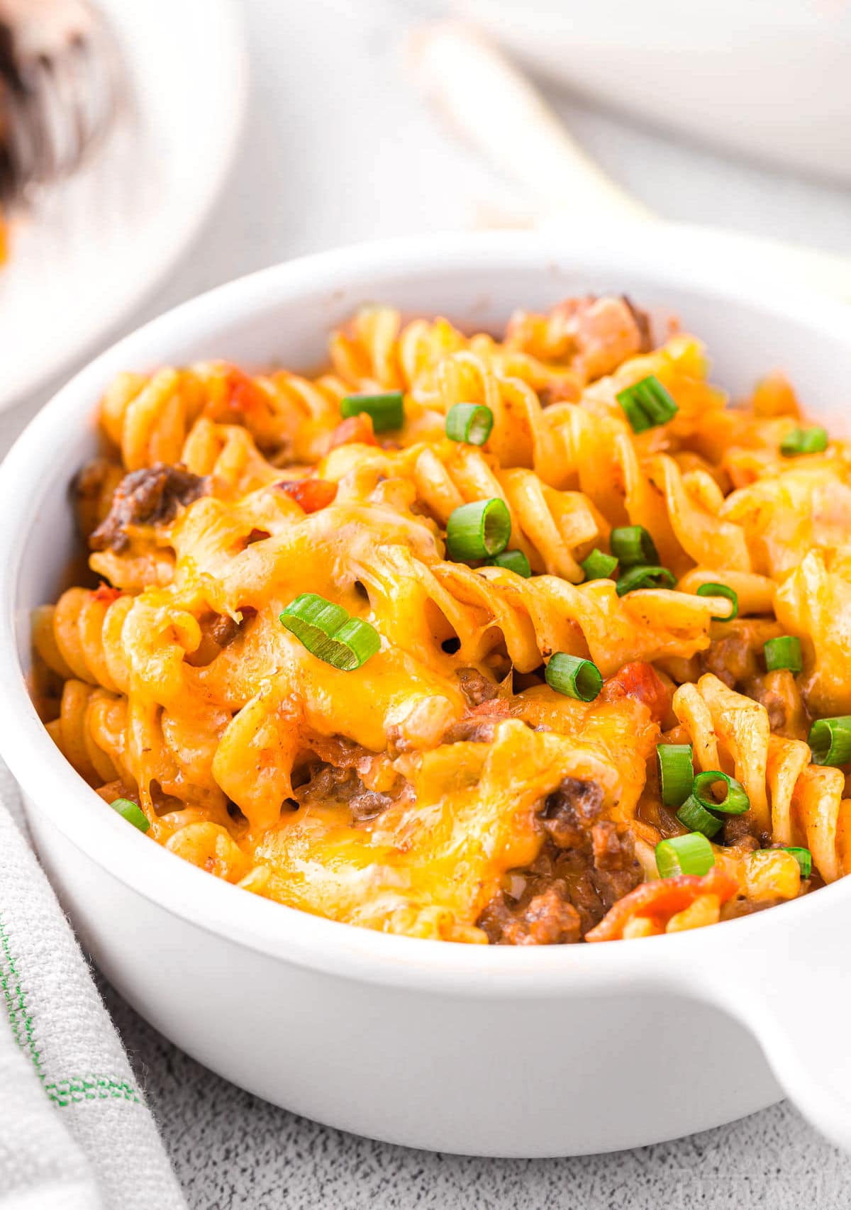 single serving of cheeseburger casserole in small white bowl with chopped green onions sprinkled on top.