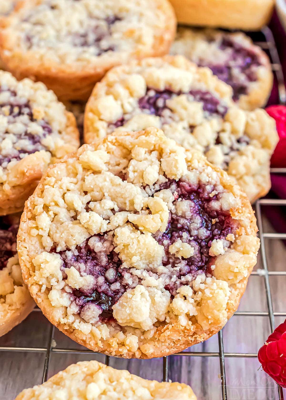 close up look at raspberry tartlet sitting up against a stack of more raspberry cookies.