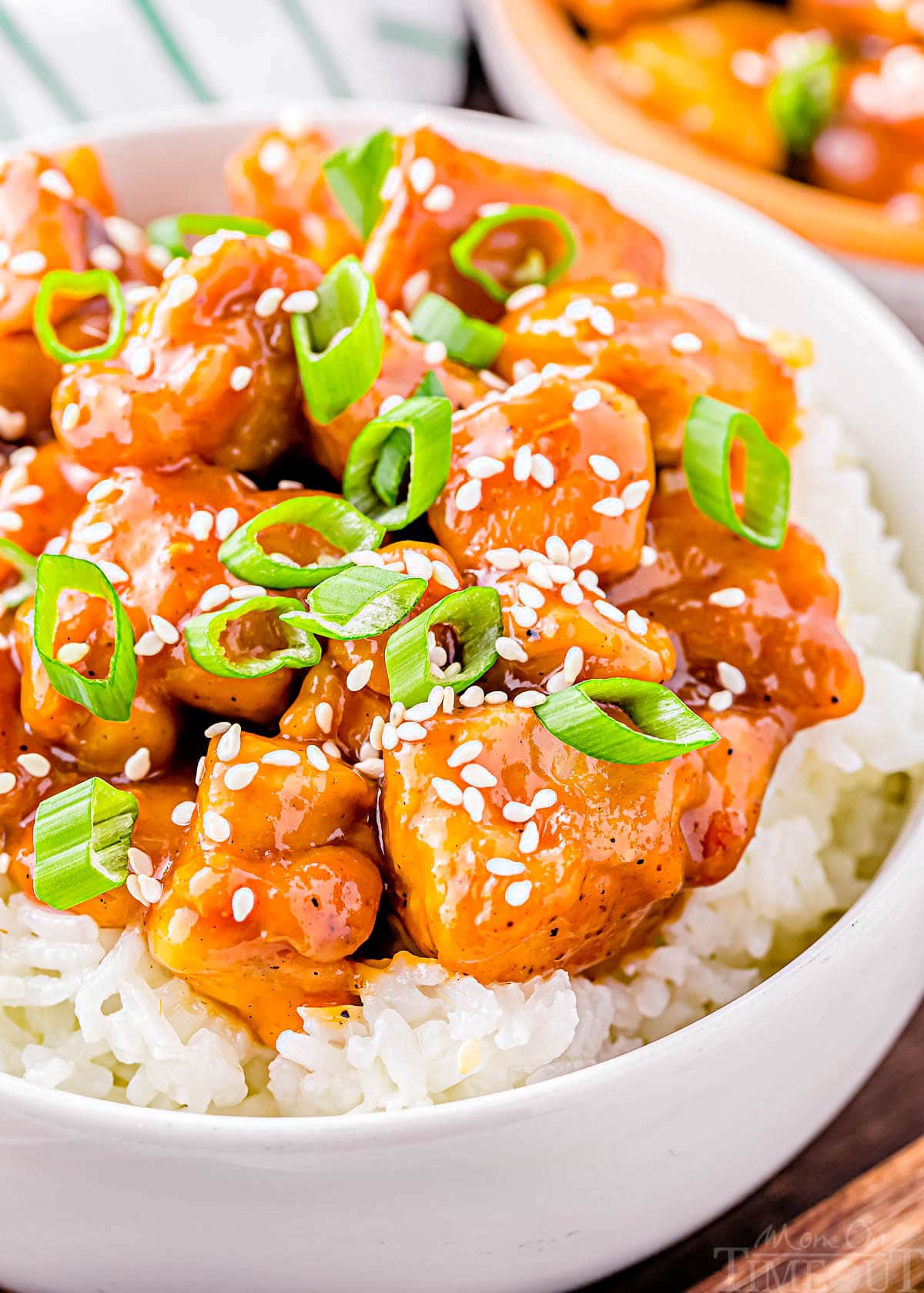 close up look at honey garlic chicken in white bowl with white rice. chicken is garnished with sliced green onions and white sesame seeds.