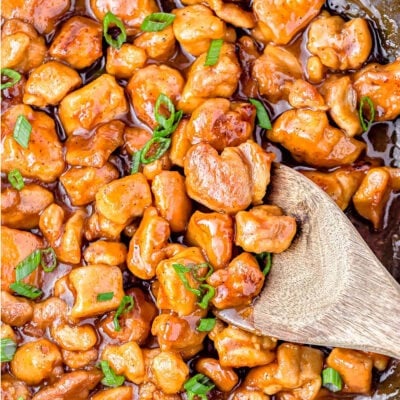 top down look at honey garlic chicken in large black skillet. wood serving spoon in skillet ready to serve the honey chicken.