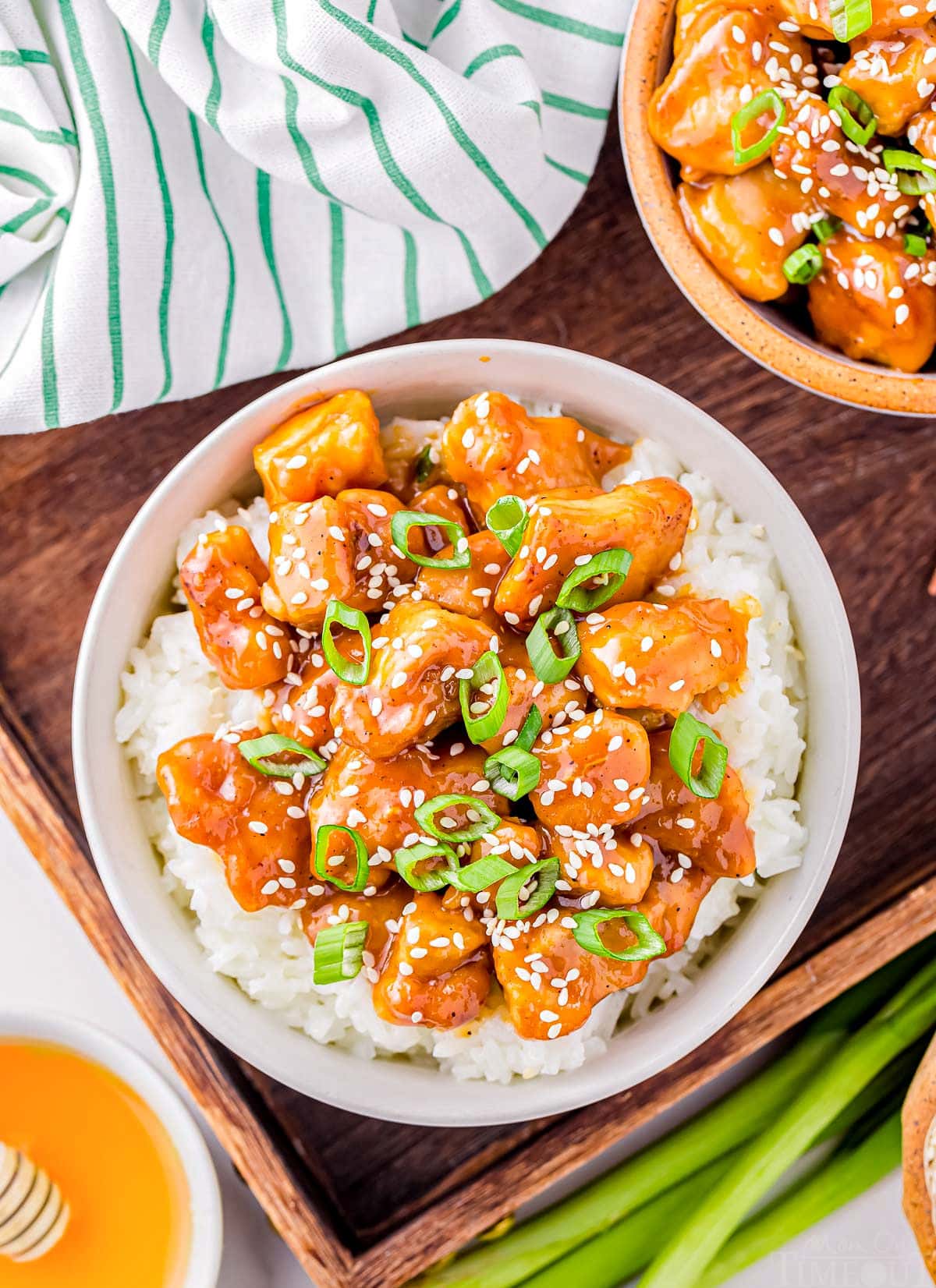 top down look at white bowl filled with steamed white rice and topped with honey garlic chicken. bowl is garnished with sesame seeds and sliced green onions.