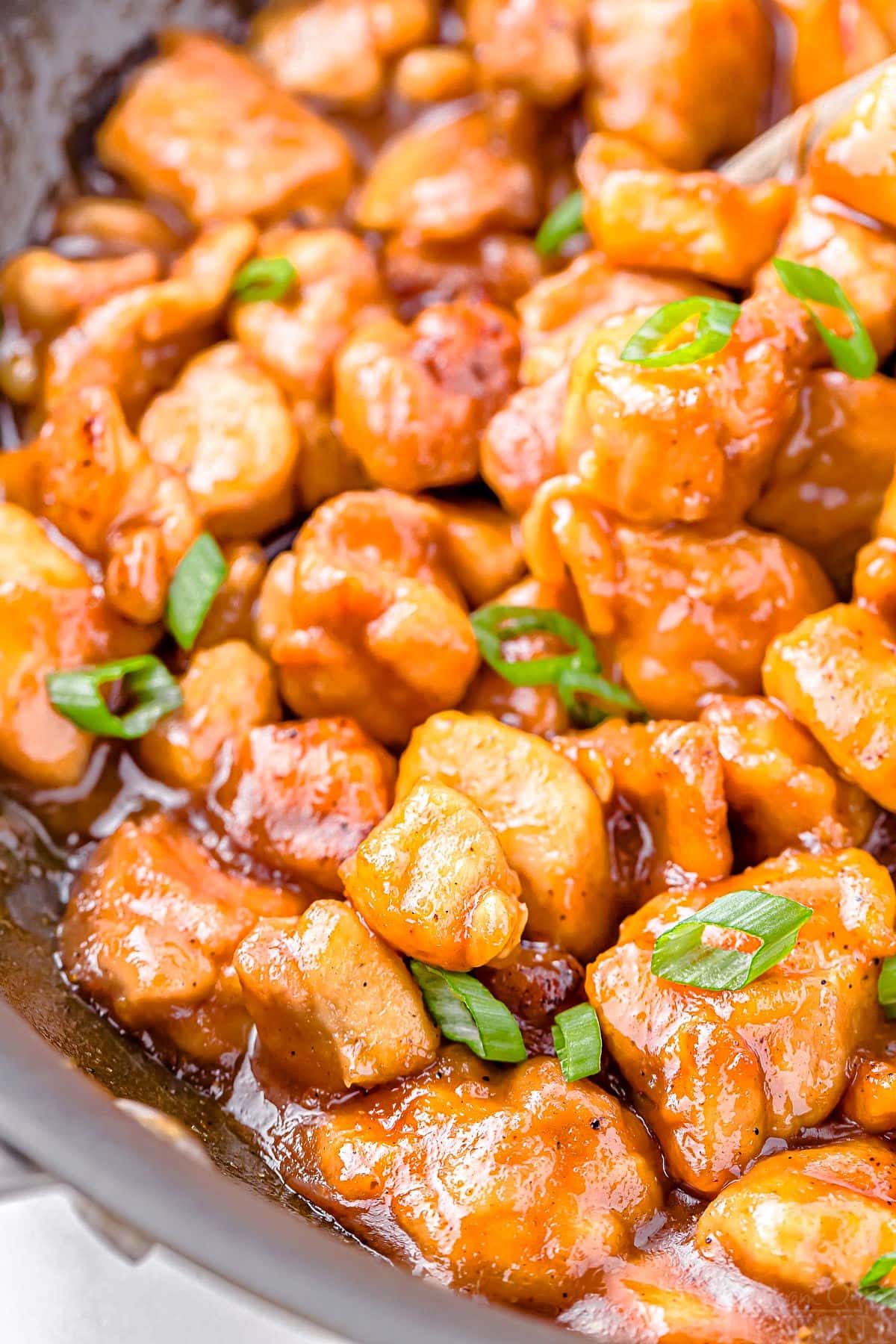 close up of honey chicken recipe in skillet garnished with green onion and nice and saucy.