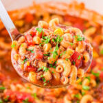 ladle full of macaroni soup held above a white dutch oven full of hamburger macaroni soup.