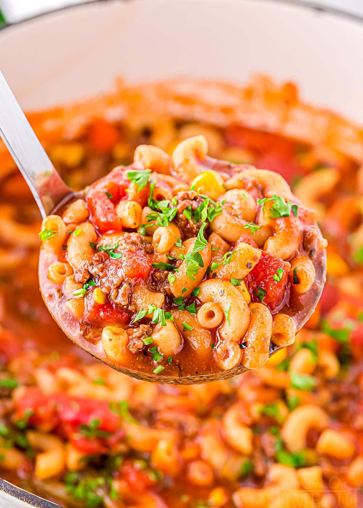 ladle full of macaroni soup held above a white dutch oven full of hamburger macaroni soup.