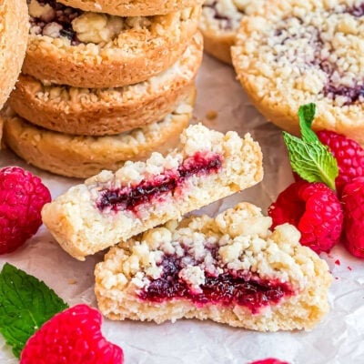 stack of costco raspberry crumble cookies with one cookie broken in half laying in front next to fresh raspberries.,