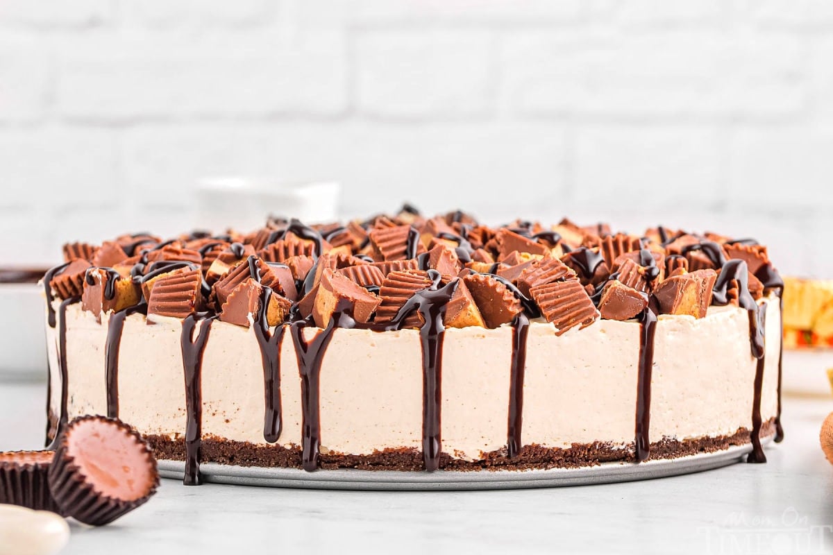 whole peanut butter cheesecake topped with reese's and fudge sitting on white surface ready to be enjoyed.