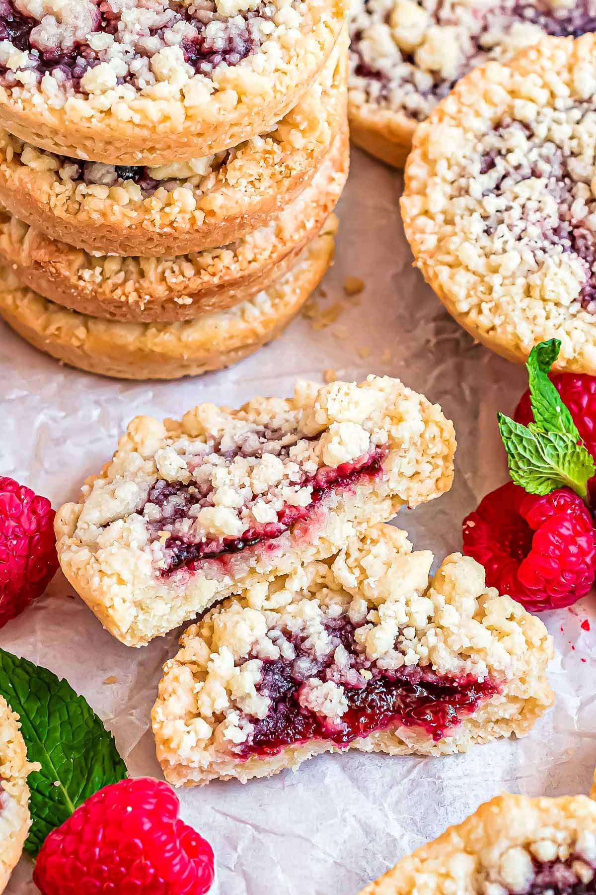 stack of costco raspberry crumble cookies with one cookie broken in half laying in front next to fresh raspberries.,